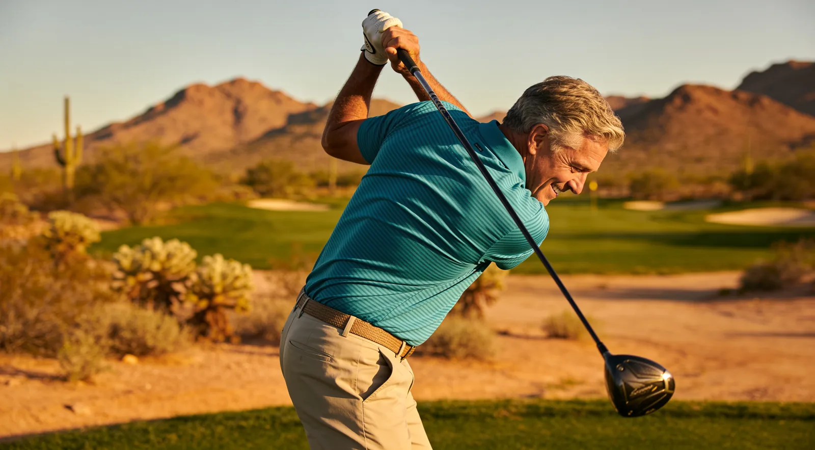 Man completing a full golf swing on a desert course
